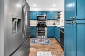 A kitchen with stainless steel appliances, blue cabinets, and a patterned rug. - Pinnacle Port C3-701 (Panama City Beach)