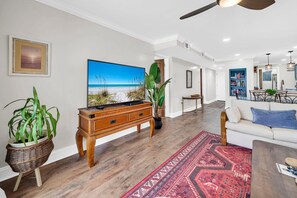A living room with a large flat-screen TV, a wooden cabinet, a red patterned rug, and a white sofa. - Pinnacle Port C3-701 (Panama City Beach)