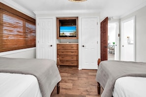 Ein Zimmer mit zwei Betten, einem hölzernen Schminktisch, einem darüber montierten Fernseher und Meerblick durch das Fenster.