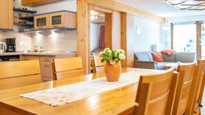 A wooden dining table with chairs, a vase with flowers, and a kitchen in the background. - Apartment 'Buche' with Shared Terrace, Shared Garden and Wi-Fi (Sankt Georgen im Schwarzwald)