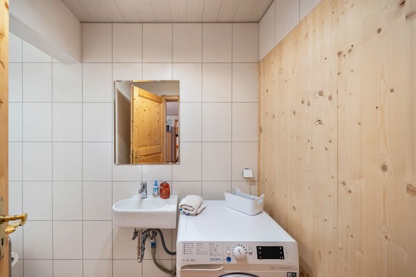 A bathroom with a white sink, a mirror, a wooden wall, and a washing machine. - Apartment 'Buche' with Shared Terrace, Shared Garden and Wi-Fi (Sankt Georgen im Schwarzwald)