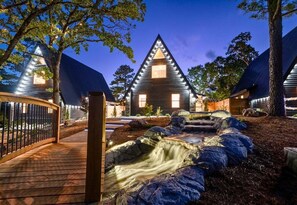 A modern building with a triangular roof, a wooden deck, and a small waterfall feature. - New Modern A-Frame Cabin w/Pool Near Hot Springs (Garland County)