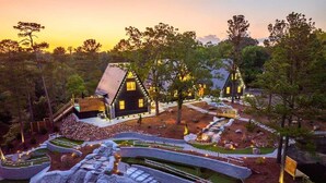 A modern house with a unique architectural design, surrounded by a landscaped garden with pathways and a small waterfall feature. - New Modern Cabin with Pool, Sauna, and Cold Plunge (Garland County)