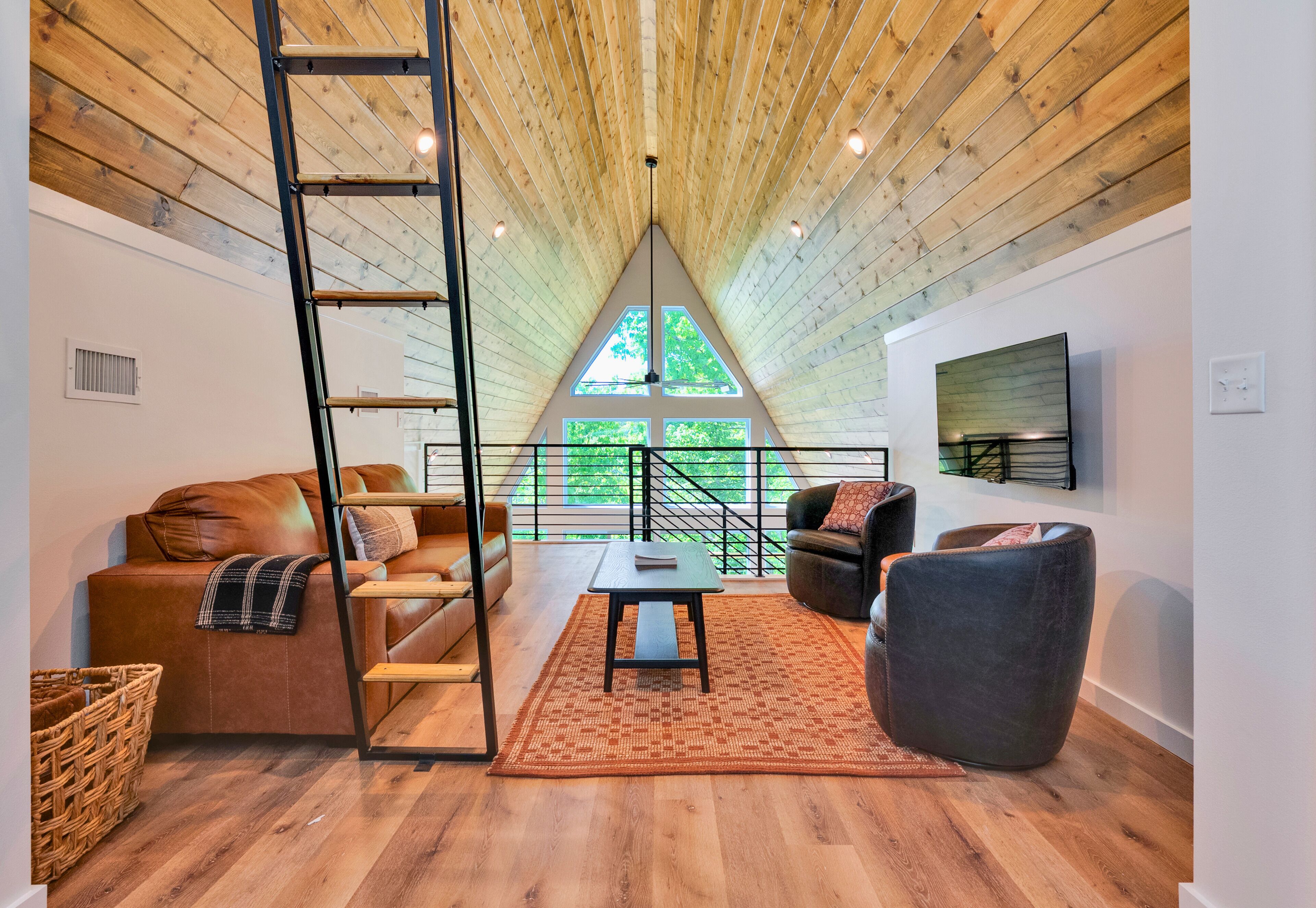 Un loft spacieux avec un plafond haut, un lit en mezzanine, un canapé, une table basse et une vue sur la verdure environnante.