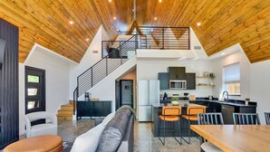 A loft-style living space with a kitchen, dining area, and a staircase to an upper level. - New Modern Cabin with Pool, Sauna, and Cold Plunge (Garland County)
