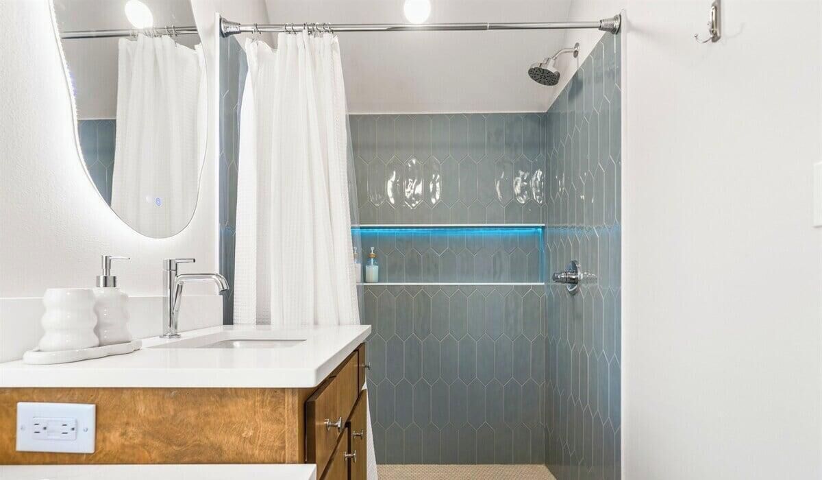 A bathroom with a shower, a sink with a mirror, and a vanity with a wooden cabinet.