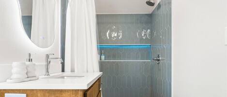A bathroom with a shower, a sink with a mirror, and a vanity with a wooden cabinet.