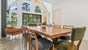 A spacious dining area with a large wooden table and chairs, large windows offering views of the outdoors, and a modern interior design. - Stylish A-Frame Getaway with Pool and Lake Access (Garland County)