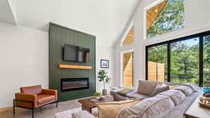 A modern living room with a fireplace, a large sofa, and a television mounted on a green wall. - Stylish A-Frame Getaway with Pool and Lake Access (Garland County)