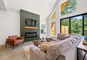 A modern living room with a fireplace, a large sofa, and a television mounted on a green wall. - Stylish A-Frame Getaway with Pool and Lake Access (Garland County)