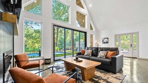 A spacious living area with a large window, a sofa, a coffee table, and a fireplace. - 3 Side-By-Side Modern Lakefront A-Frame Cabins (Garland County)