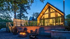 A modern cabin with a large window, a fire pit, and outdoor seating. - 3 Side-By-Side Modern Lakefront A-Frame Cabins (Garland County)
