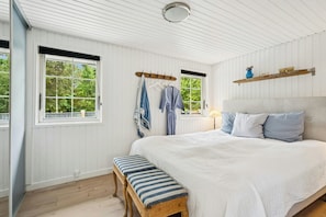 Ein Schlafzimmer mit einem großen Bett, einer Holzbank, zwei Fenstern mit Vorhängen und einem Regal mit Dekoration.