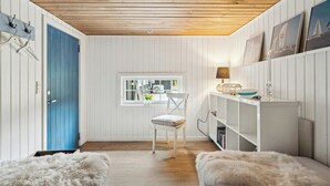 Een kamer met een houten plafond, een blauwe deur, een witte stoel, een kleine tafel en een boekenkast.