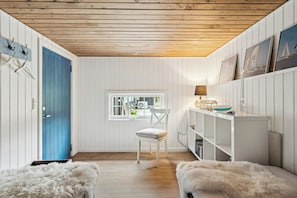 Ein Zimmer mit Holzboden, einer blauen Tür, einem weißen Stuhl, einem kleinen Tisch und einem Bücherregal.