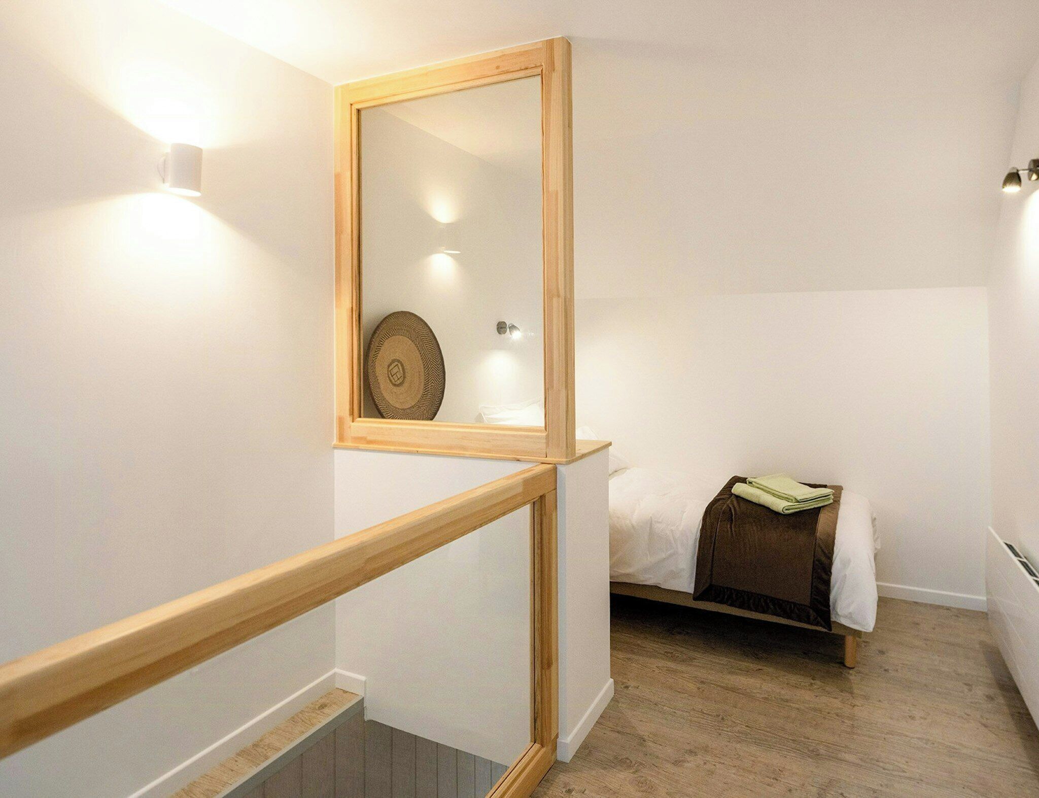 A bedroom with a wooden-framed mirror, a bed with a brown headboard, and a small bedside table with a folded towel.