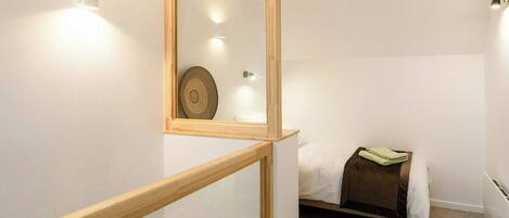 A bedroom with a wooden-framed mirror, a bed with a brown headboard, and a small bedside table with a folded towel.