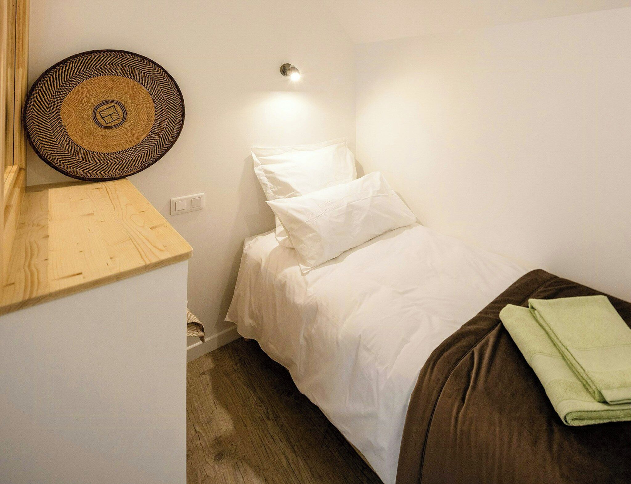 Una habitación pequeña y ordenada con una cama individual, una lámpara fijada a la pared y un tapiz de pared tejido.