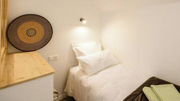 Una habitación pequeña y ordenada con una cama individual, una lámpara fijada a la pared y un tapiz de pared tejido.