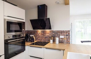 Eine Küche mit Backsteinwand, einer Mikrowelle, einem Backofen, einer Kaffeemaschine und einem Fenster.