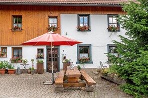 Een houten gebouw met een binnenplaats, een rode parasol, een houten bank en potplanten.