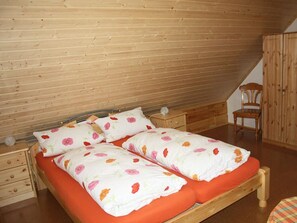 A bedroom with a wooden sloped ceiling, a double bed with floral bedding, a nightstand, a chair, and a wardrobe.