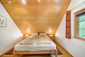 Een slaapkamer met een houten plafond, een bed met bloemenbedrukking, een nachtkastje met een lamp en een raam met gordijn.