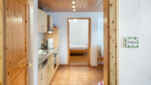 Un corridoio stretto con porte in legno, una zona cucina con mobili ed elettrodomestici, e un letto sullo sfondo.