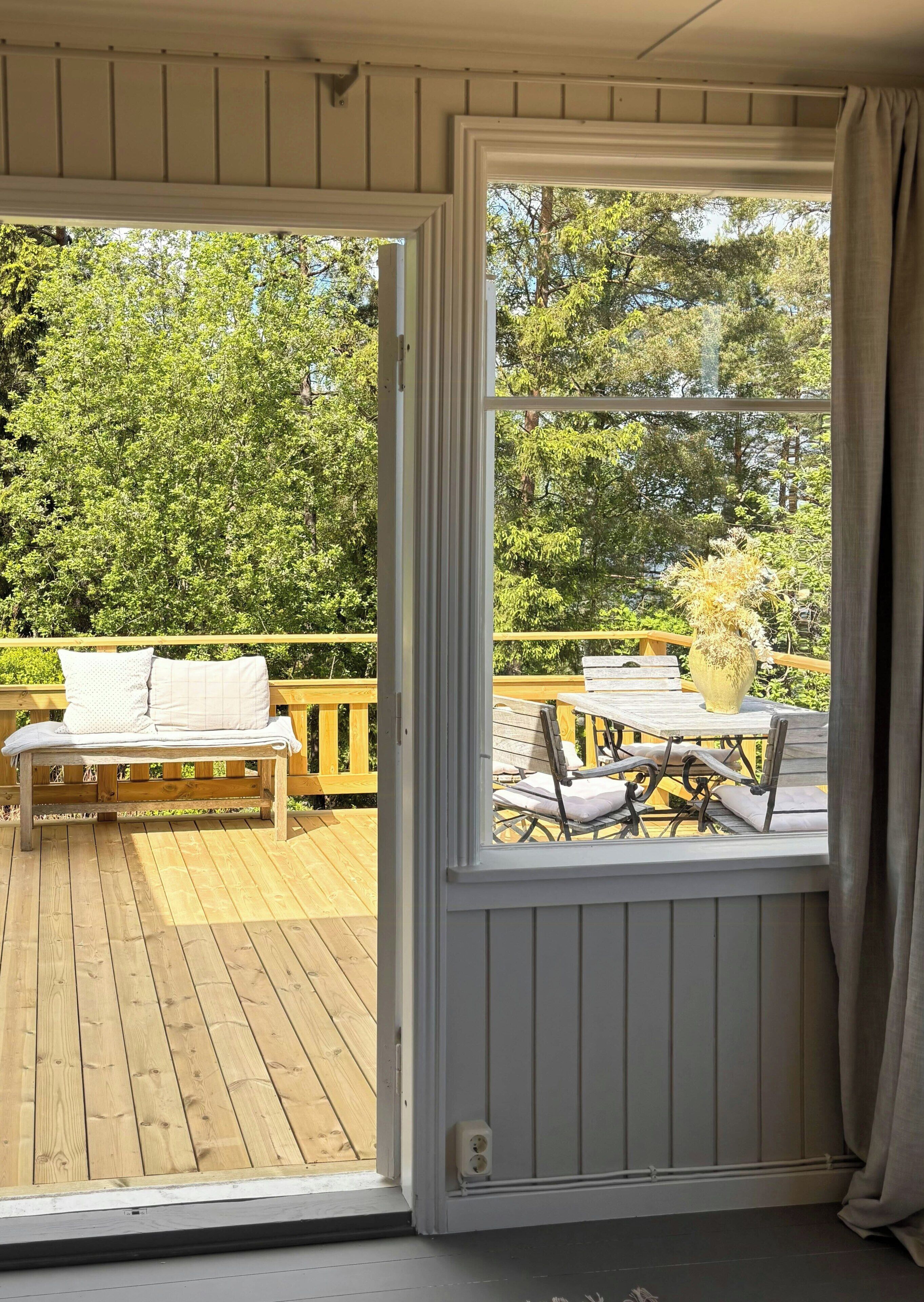 An open sliding door to a deck with a wooden bench and a table with chairs.