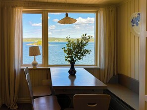 Ein Essbereich mit Tisch, Stühlen, einer Vase mit Grünpflanzen, einer Lampe und Blick aufs Wasser.
