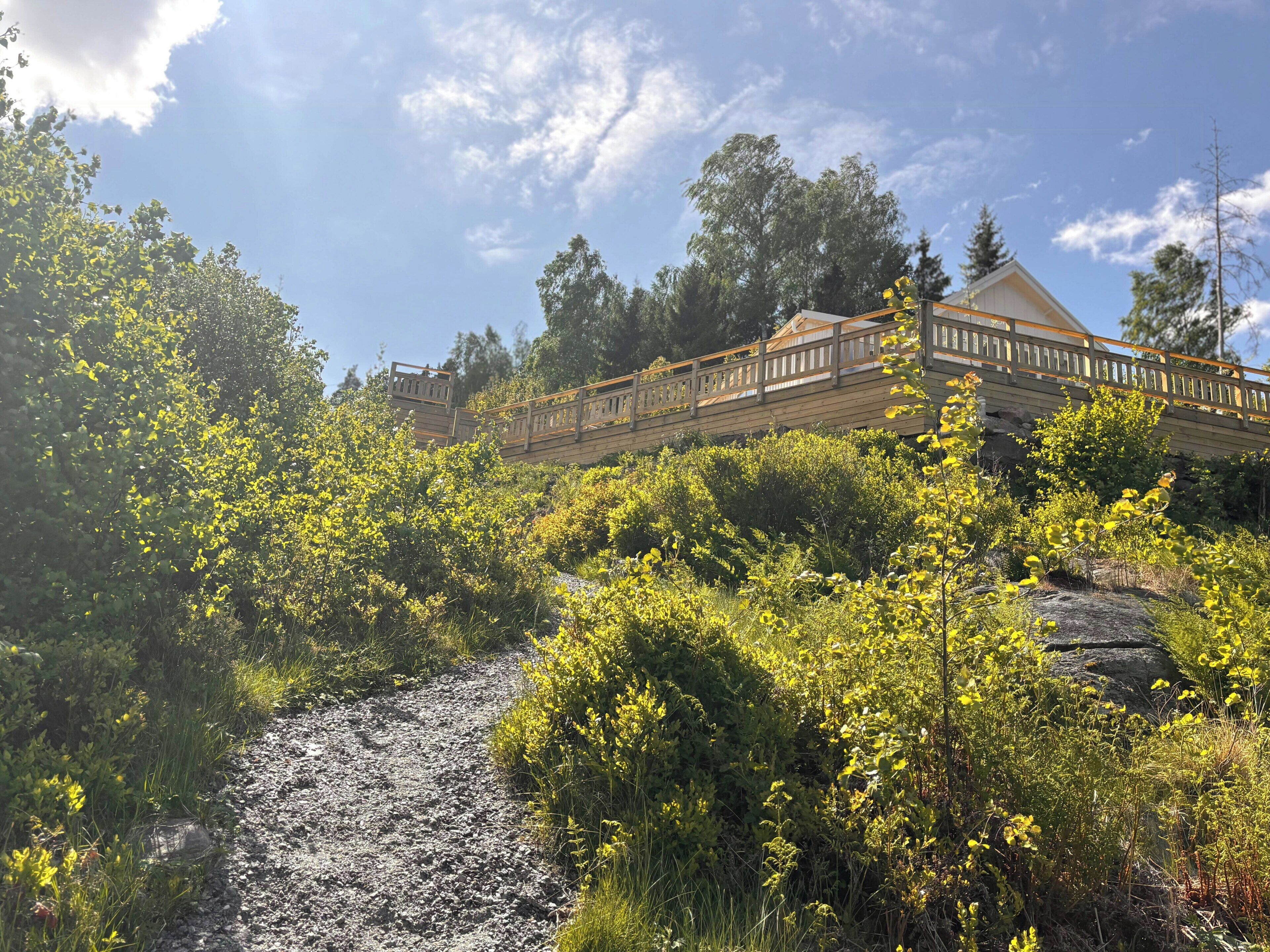 A wooden bridge over a gravel path, surrounded by dense greenery and trees.