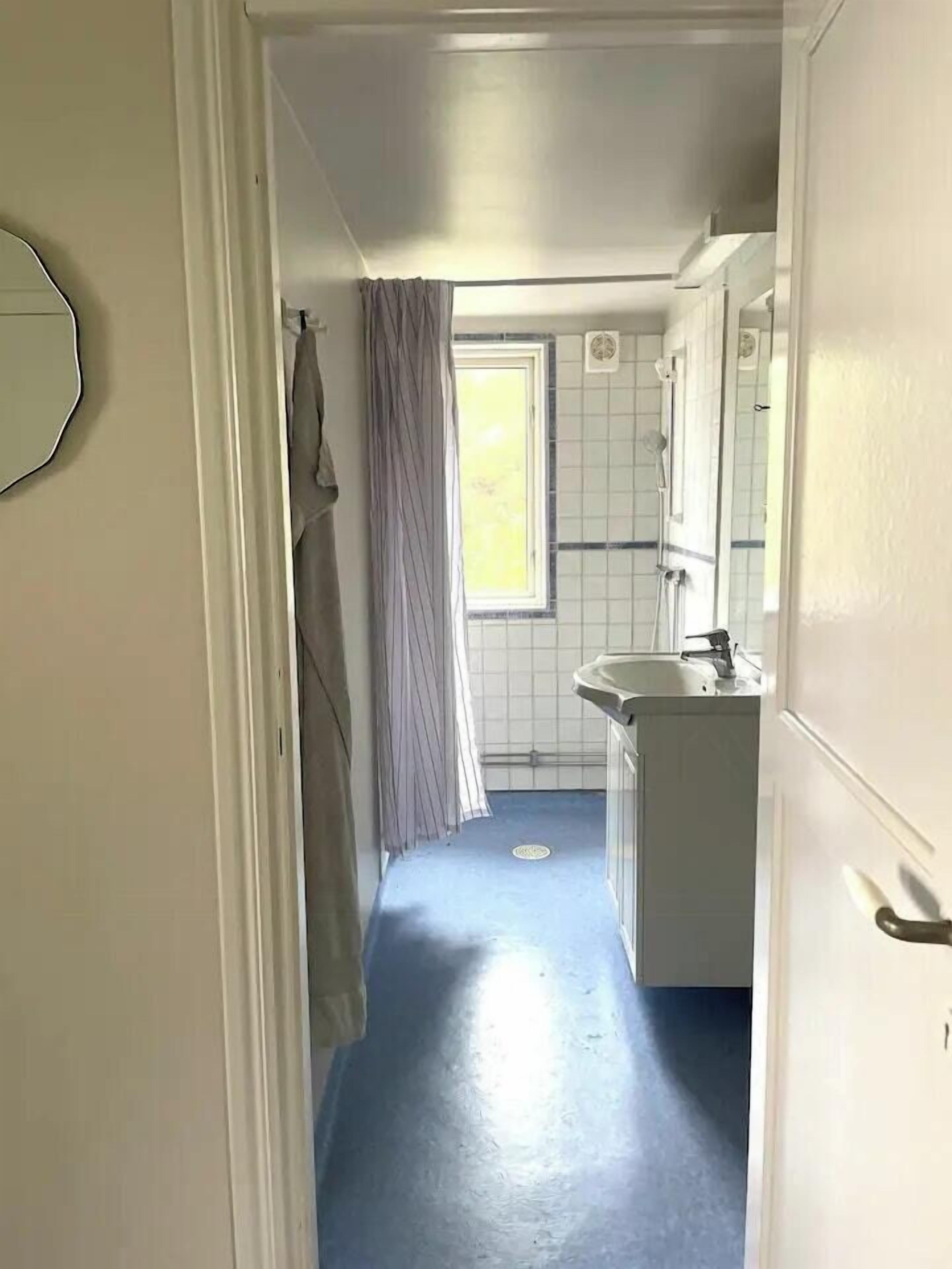 A narrow hallway leading to a bathroom with a window, a sink, and a mirror.