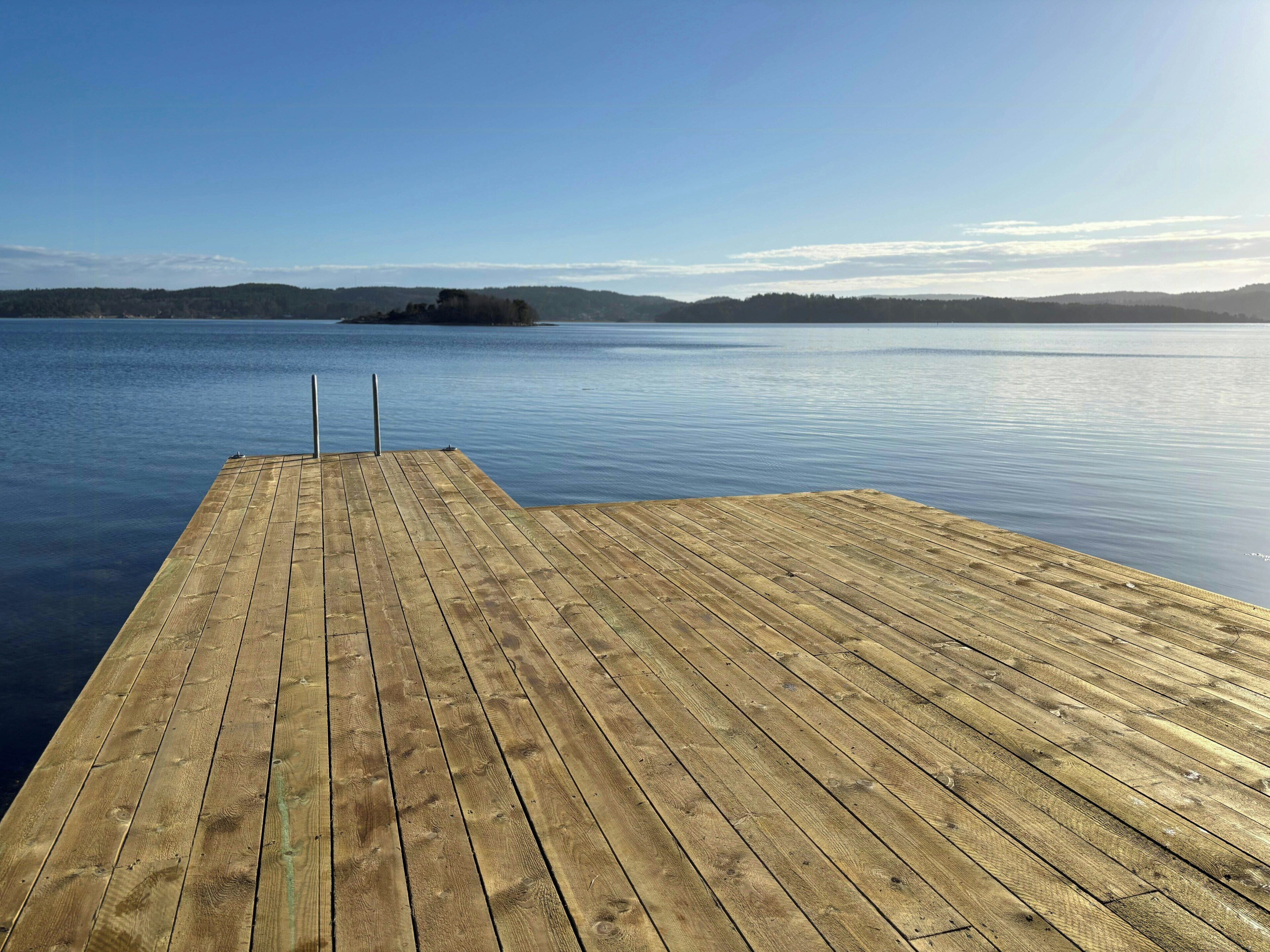A wooden dock extending into calm water with a clear sky and distant land.