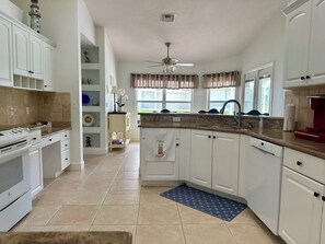 A kitchen with white cabinets, a built-in oven, a microwave, a sink, and a ceiling fan.