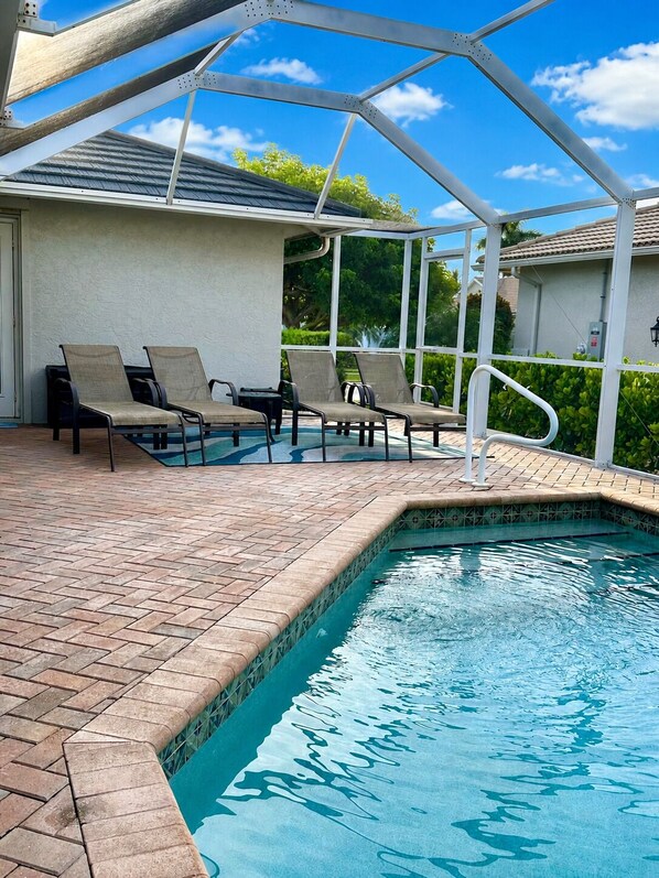 A swimming pool with a covered area, lounge chairs, and a tiled deck.