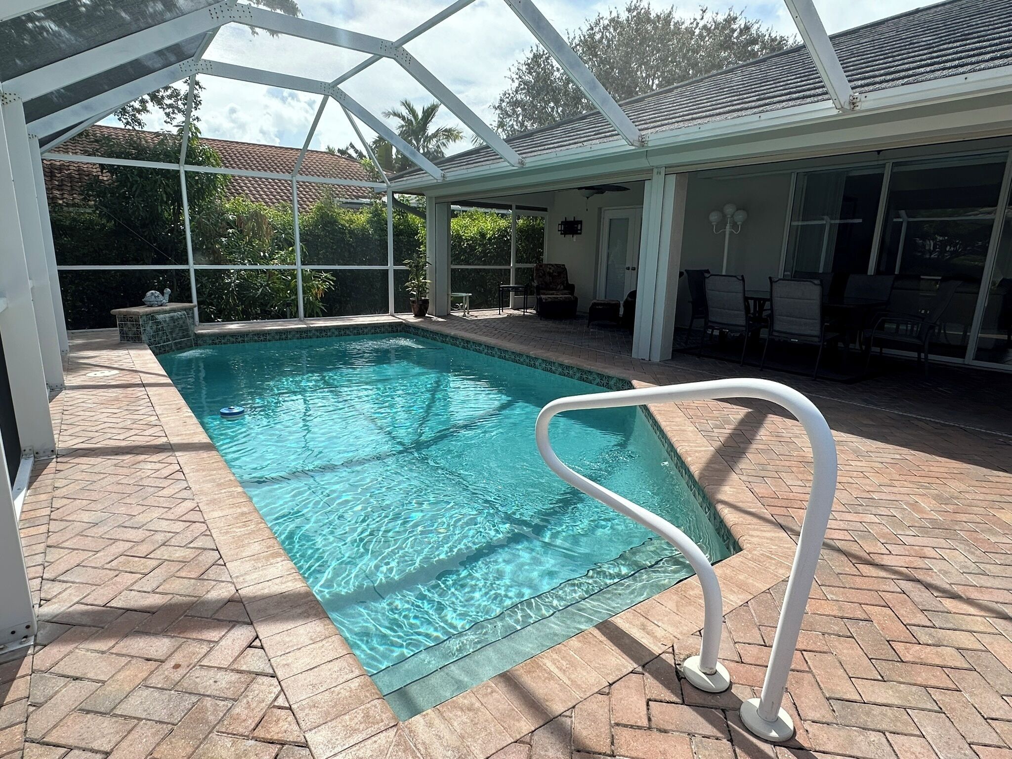 Ein überdachter Innenbereich mit Schwimmbad und klarem Wasser, umgeben von einer Veranda mit Stühlen und Tischen.