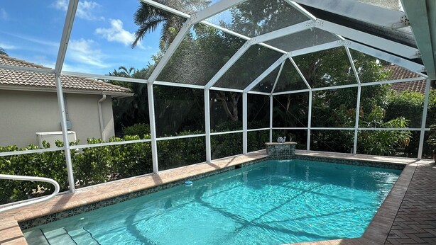 Una piscina con superficie de agua azul cristalina, rodeada por un patio de ladrillo y un cerramiento de vidrio.