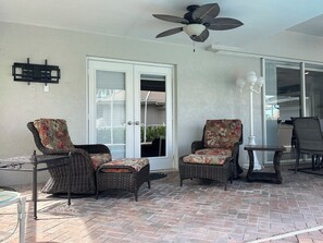 A covered patio area with wicker furniture, a ceiling fan, and a sliding glass door leading to a covered outdoor space.