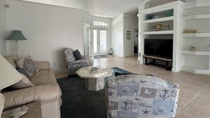 Un salón amplio con ventilador de techo, televisión y estantería.
