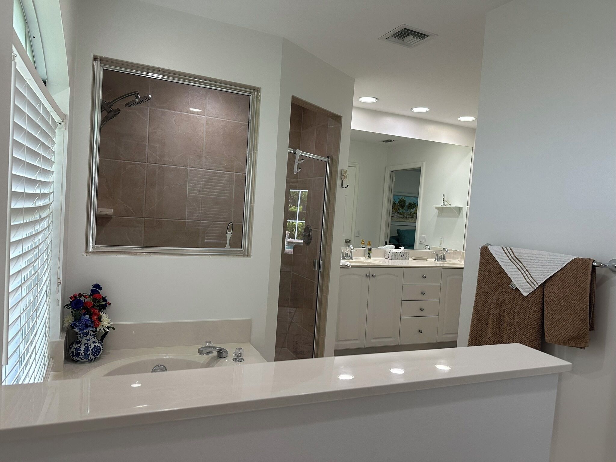 A modern bathroom with a large mirror, a shower, a vanity with a sink, and a towel rack.
