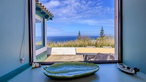 A window with a view of the ocean and a patio area with a green dish and a small boat model. - GuestReady - Casa do Horizonte (Mosteiros)