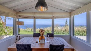 A dining area with a table, chairs, a hanging light fixture, and a view of the ocean. - GuestReady - Casa do Horizonte (Mosteiros)