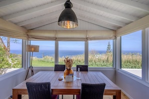 Un comedor con una mesa, sillas, una lámpara colgante y vista al océano.