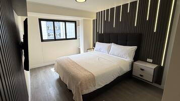A modern bedroom with a large bed, bedside tables, a window, and a view of buildings outside.