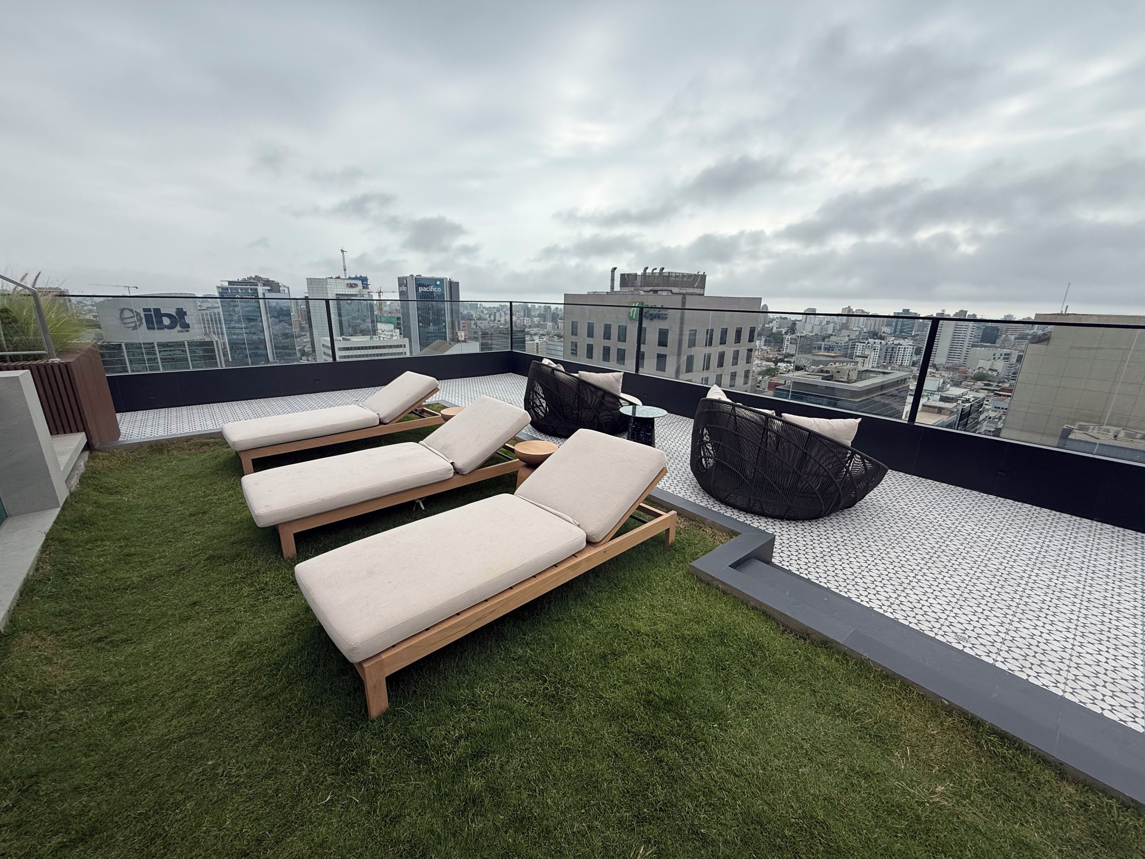 A rooftop terrace with lounge chairs, a wicker sofa, and a view of the cityscape.