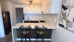 A modern kitchen with white cabinets, a central island with bar stools, a built-in oven, and a hanging light fixture. - Aparts4Days 1 Bedroom Apartment AR (Lima)