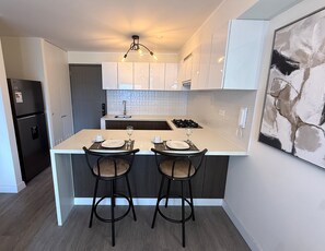 Una cocina moderna con armarios blancos, una isla central con taburetes y un horno empotrado, además de una lámpara colgante.