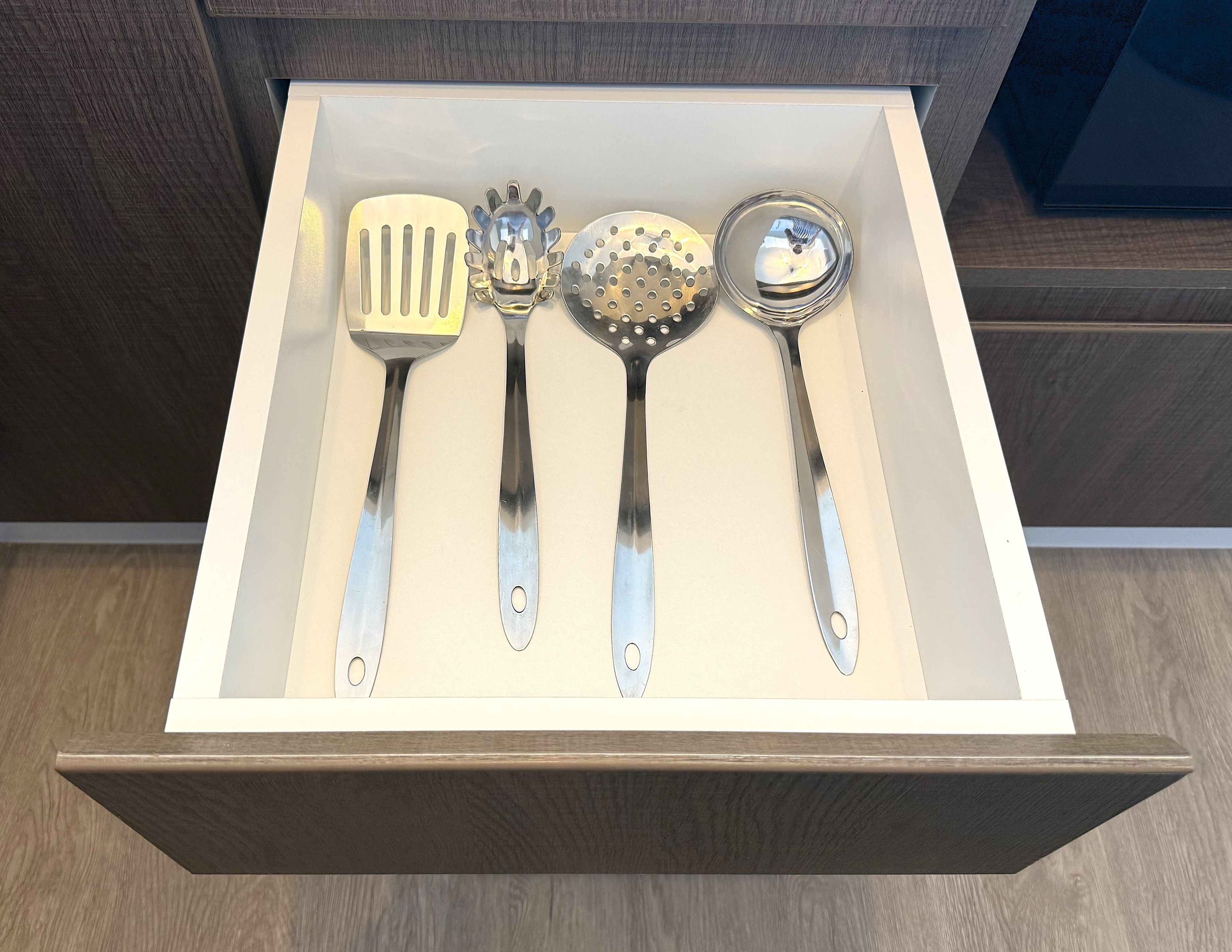 Un cajón con cuatro utensilios de cocina: una espátula, un rallador, un rallador con agujeros y una cuchara para servir.