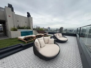 Terraza en la azotea con piscina, sillas de descanso y vistas a la ciudad.