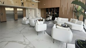 A modern lobby with a marble floor, white sofas, a coffee table, and a bookshelf. - Aparts4Days 1 Bedroom Apartment AR (Lima)